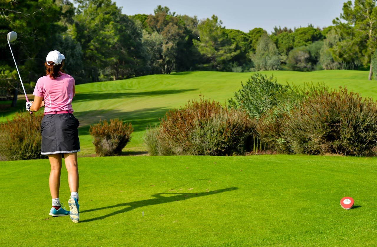 Woman playing golf on a vibrant green course with scenic tree backdrop.