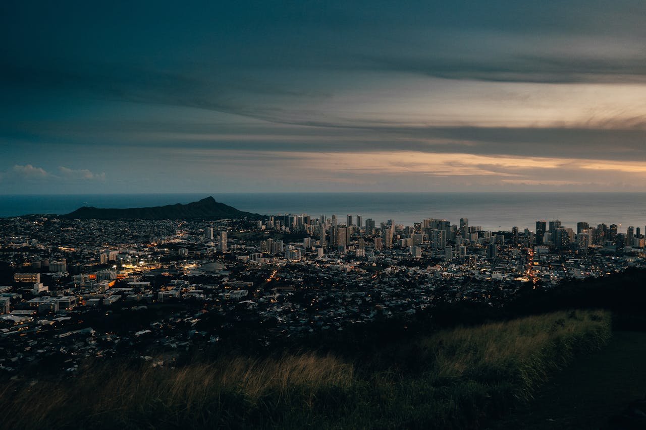 Captivating aerial view of Honolulus skyline and ocean at dusk, featuring Diamond Head and vibrant city lights.