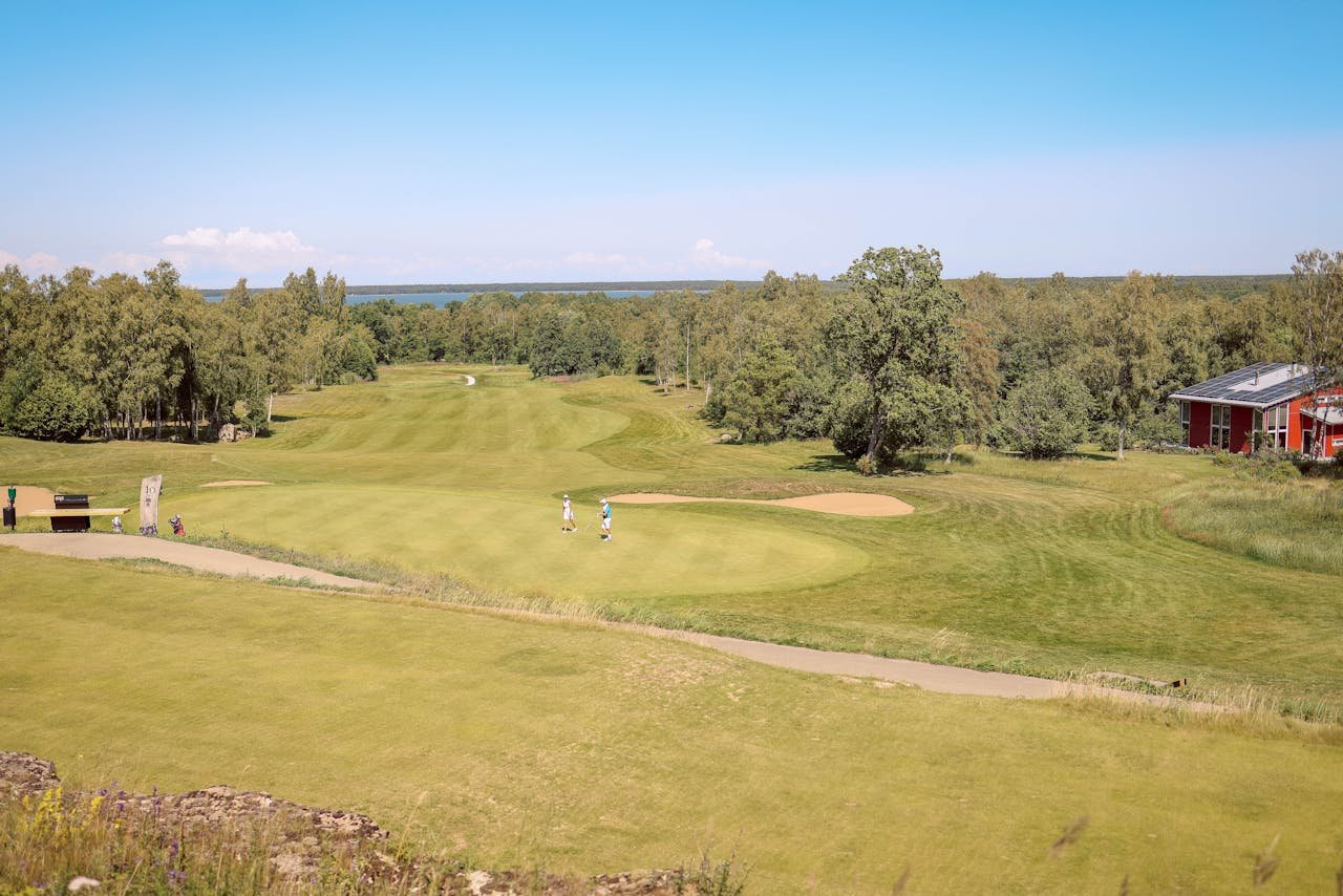Aerial view of a picturesque golf course with players, surrounded by lush greenery.